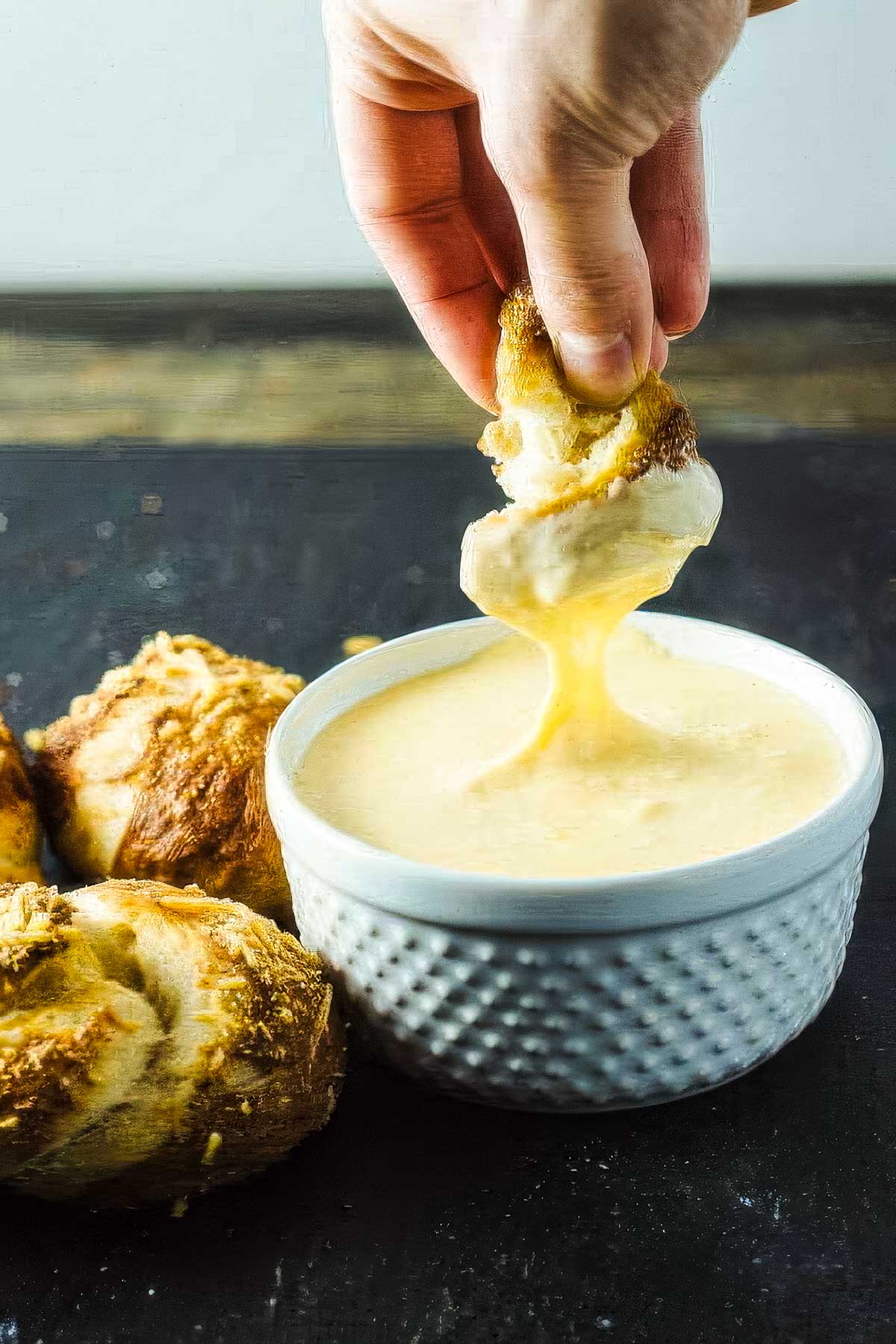 Garlic Pretzel Knots with Cheese Dipping Sauce several garlic pretzel knots next to a dish of warm cheese sauce with a person dipping