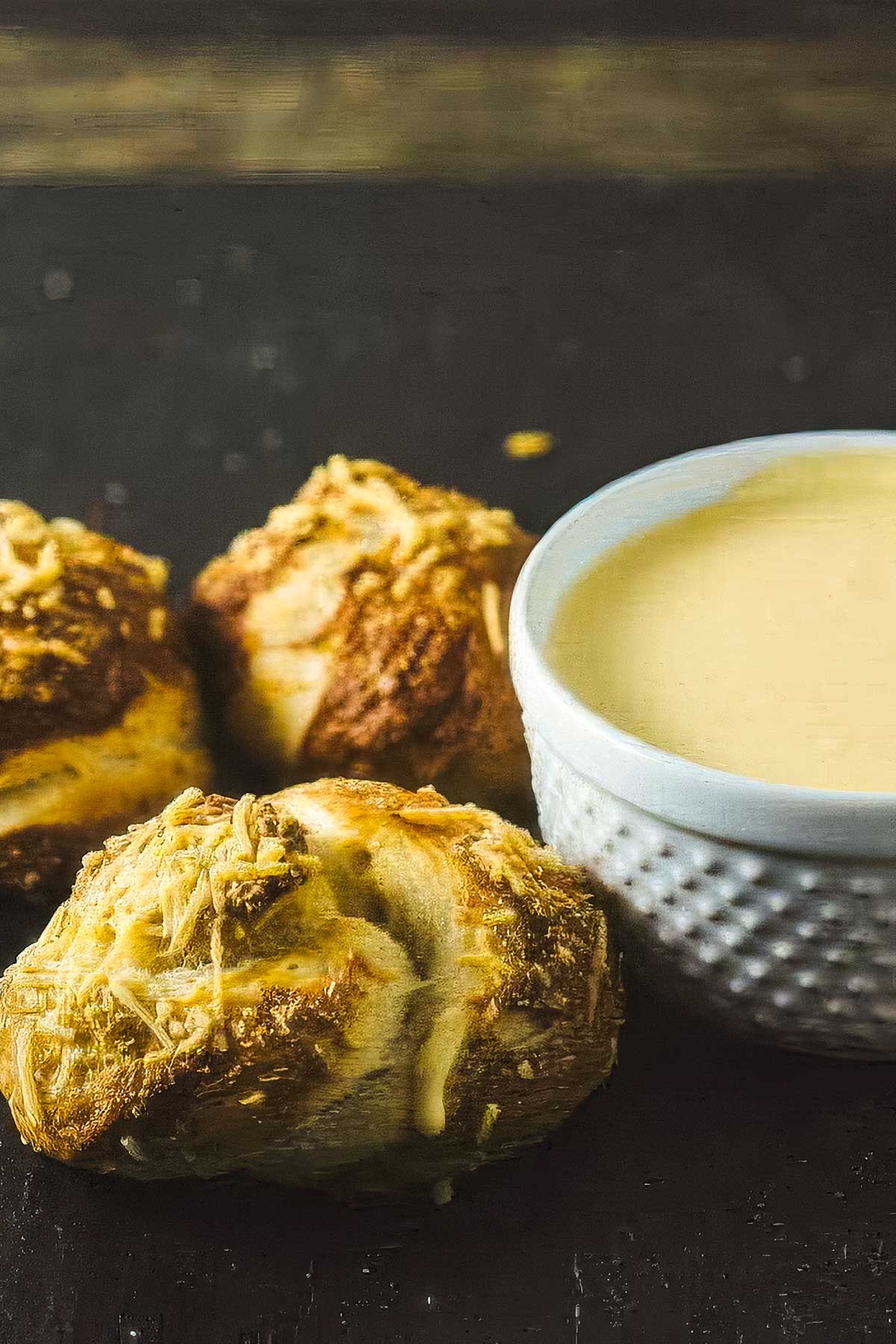 Garlic Pretzel Knots with Cheese Dipping Sauce several garlic pretzel knots next to a dish of warm cheese sauce