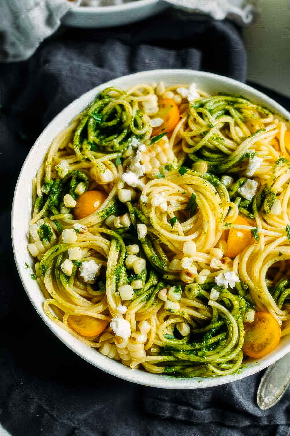 a top-down view of summer pasta salad with avocado pesto in a white bowl with swirls of spaghetti noodles