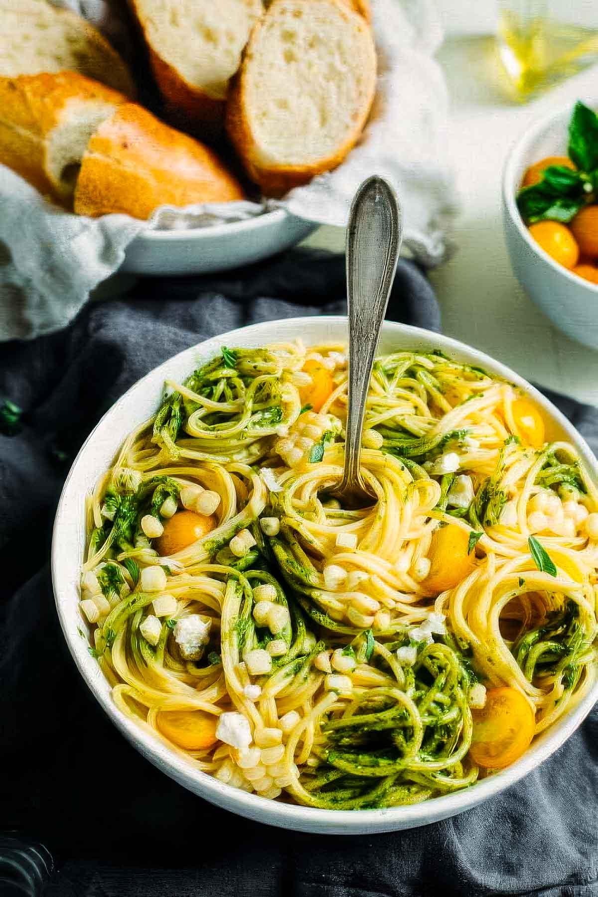 Summer Pasta Salad with Avocado Pesto a top-down view of summer pasta salad with avocado pesto in a white bowl with swirls of spaghetti noodles and a fork
