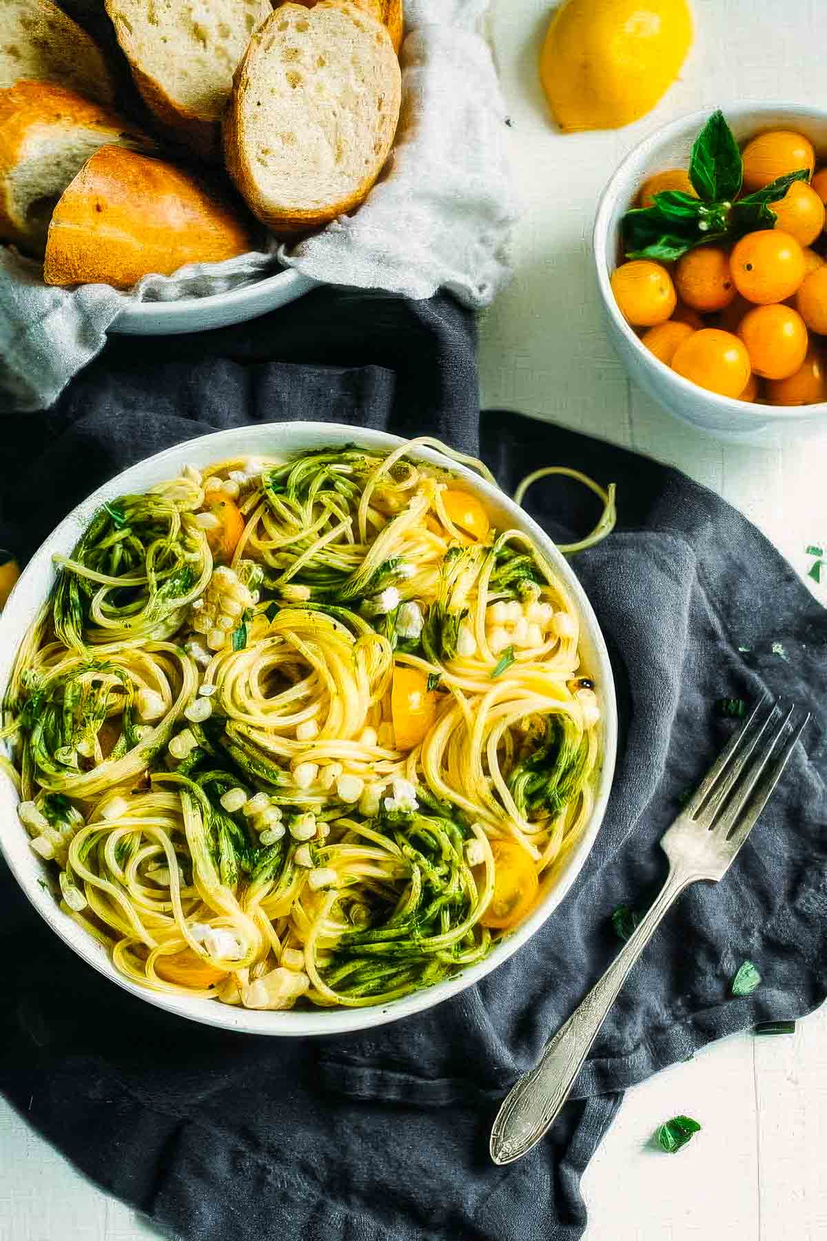 Summer Pasta Salad with Avocado Pesto a top-down view of summer pasta salad with avocado pesto in a white bowl with swirls of spaghetti noodles on a linen cloth