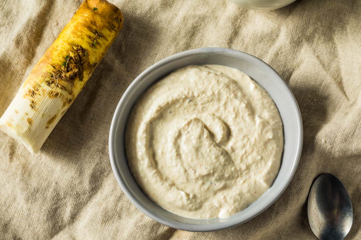 Horseradish Sauce For Prime Rib an overhead shot of a gray bowl filled with horseradish sauce on a beige napkin, next to a pepper grinder